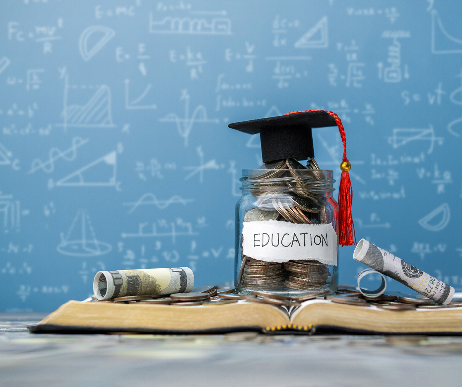 Jar of coins sitting on open text book with graduation cap